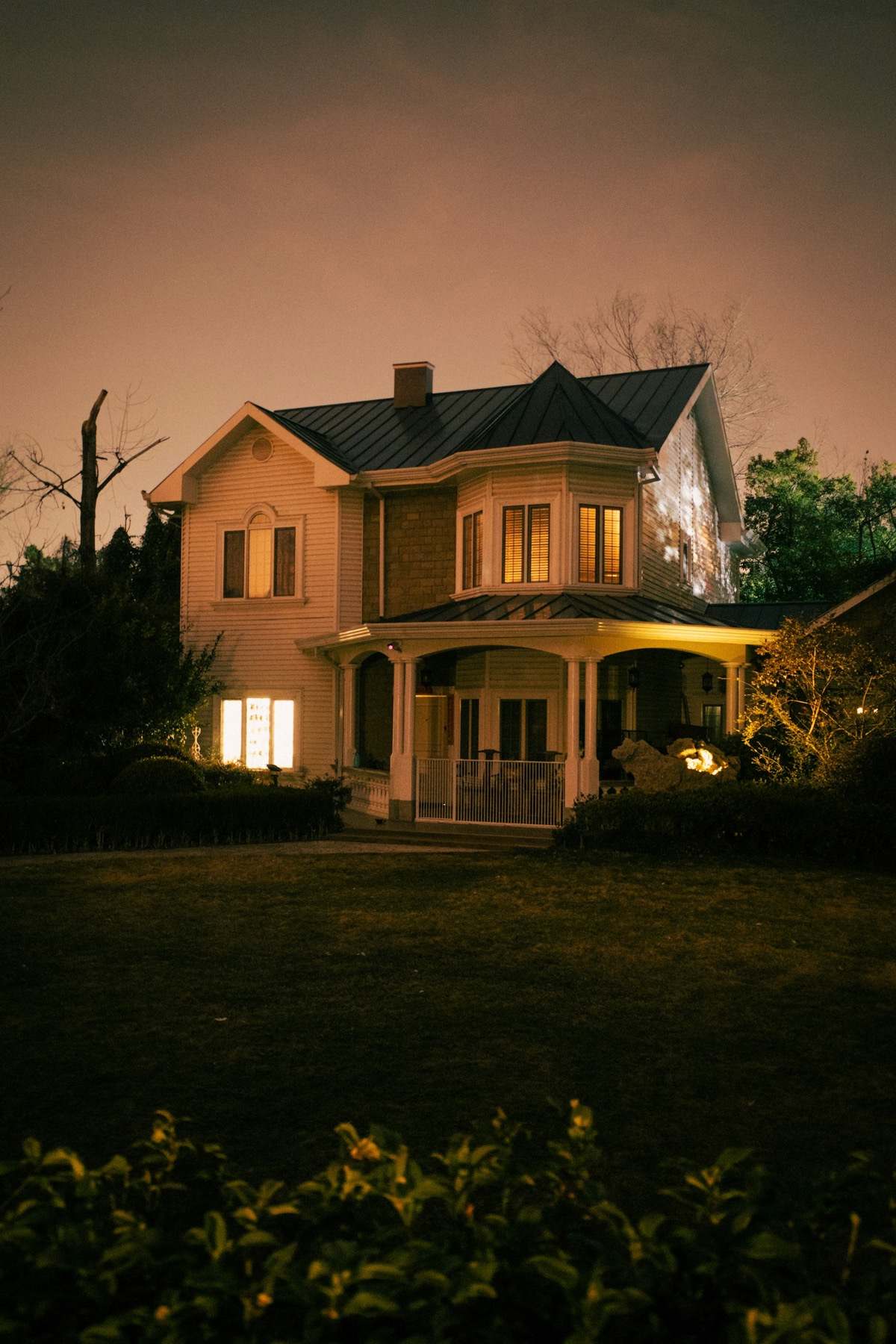 A two-storey house at dusk with warm light in its windows.